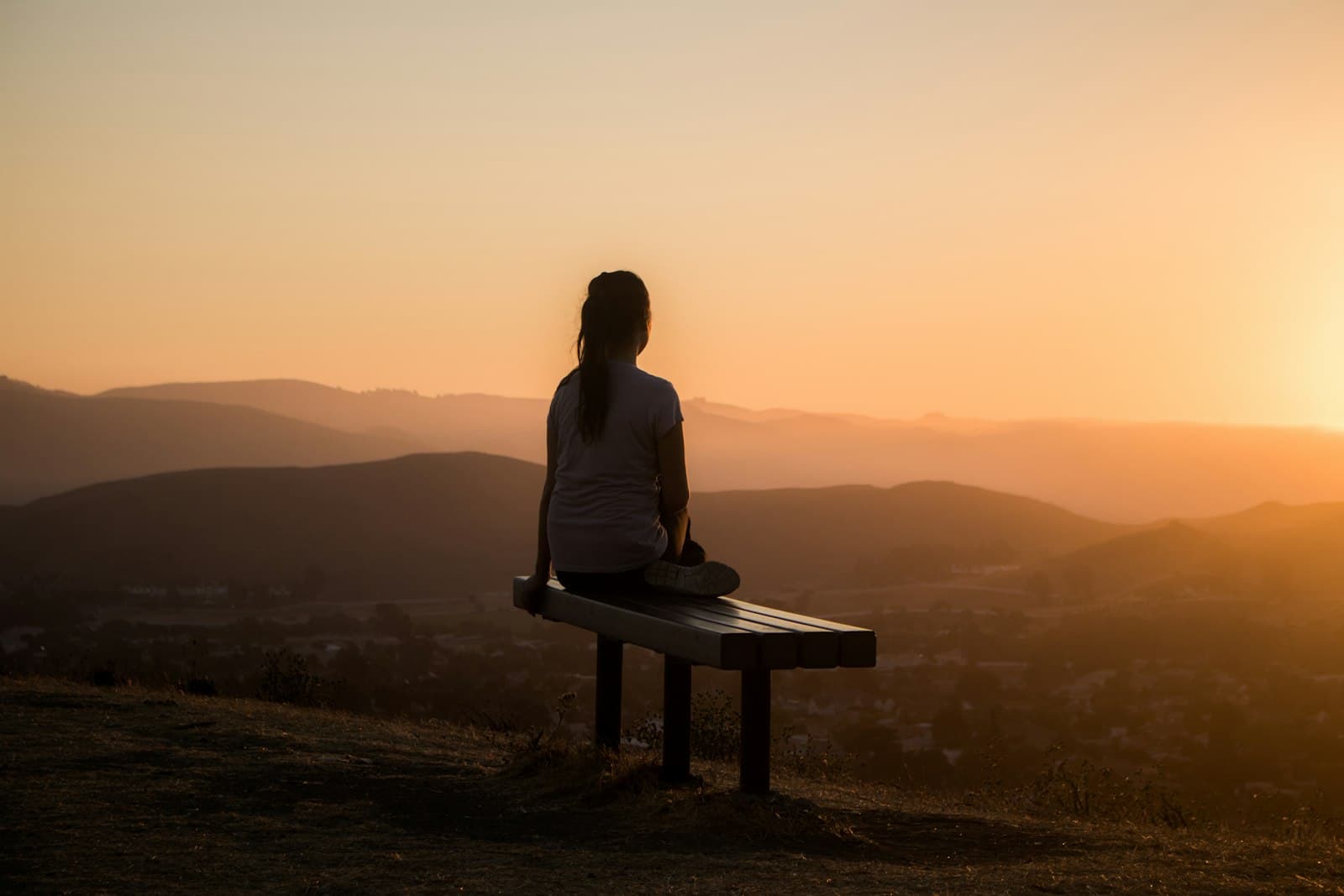 A person sitting on a bench looking out over hills at sunset