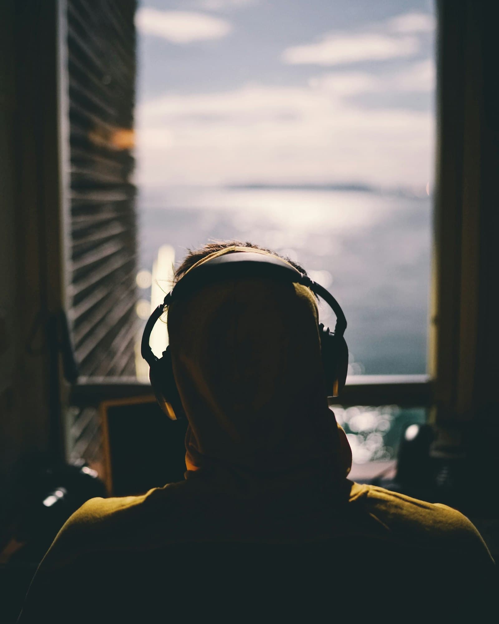 A person in headphones looking out of a window at the sea