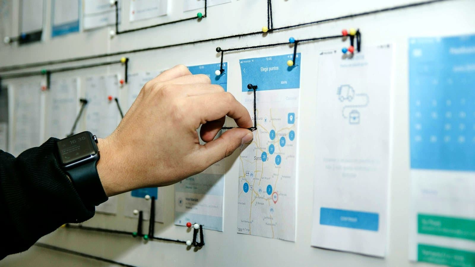 A hand connecting app screens with string on a wall, mapping how someone moves through a journey