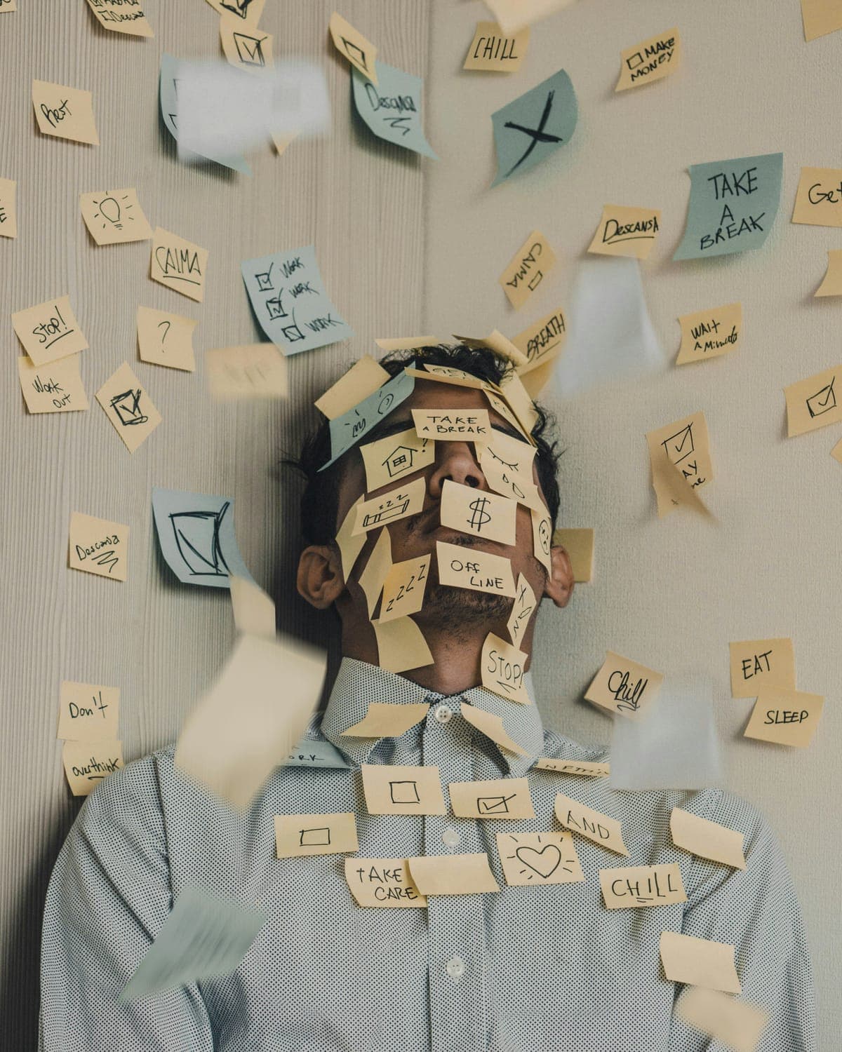 A man against a wall covered in sticky notes reading stop, take a break and do not overthink